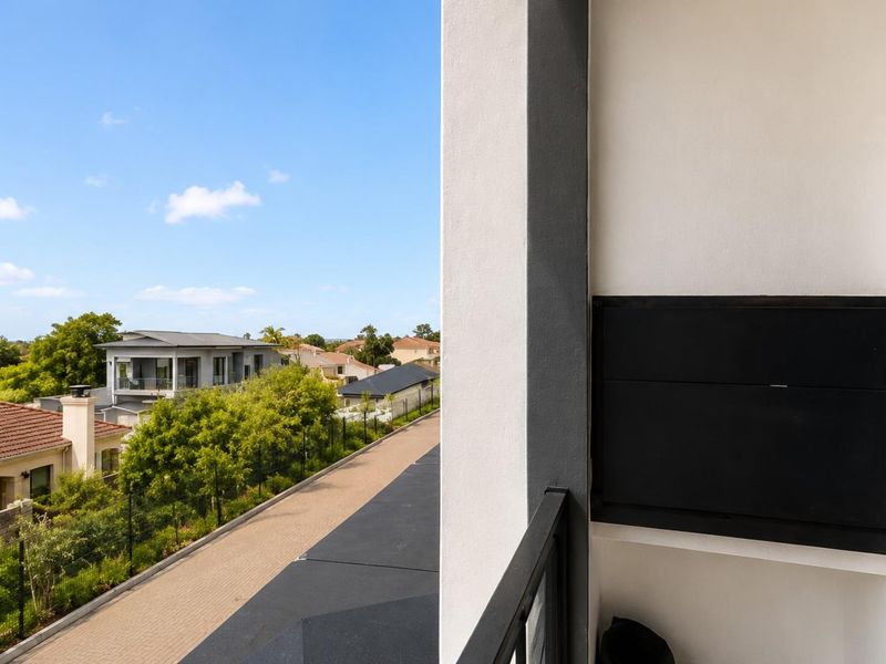 A modern balcony featuring a built-in braai, sleek metal balustrade, and elevated views over the surrounding residential estate.