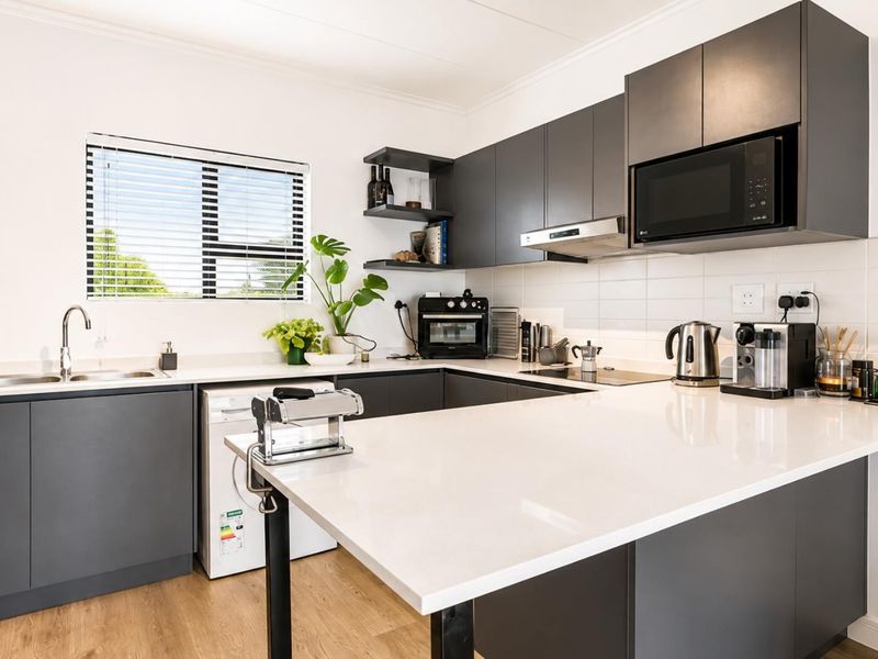 Modern kitchen featuring charcoal cabinetry, white stone countertops, tiled backsplash, and integrated appliances, offering a clean and contemporary aesthetic.