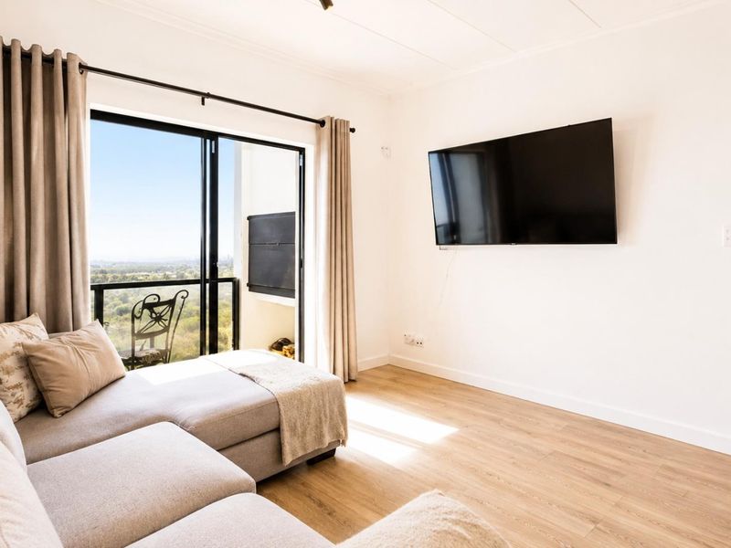 Bright living room featuring laminate flooring and a large sliding glass door providing access to a balcony with scenic views.