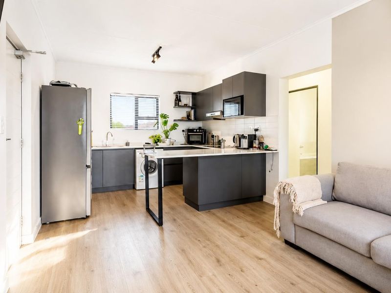 Modern open-plan living area featuring a contemporary kitchen with dark cabinetry, integrated appliances, laminate flooring, and a wall-mounted air conditioning unit.