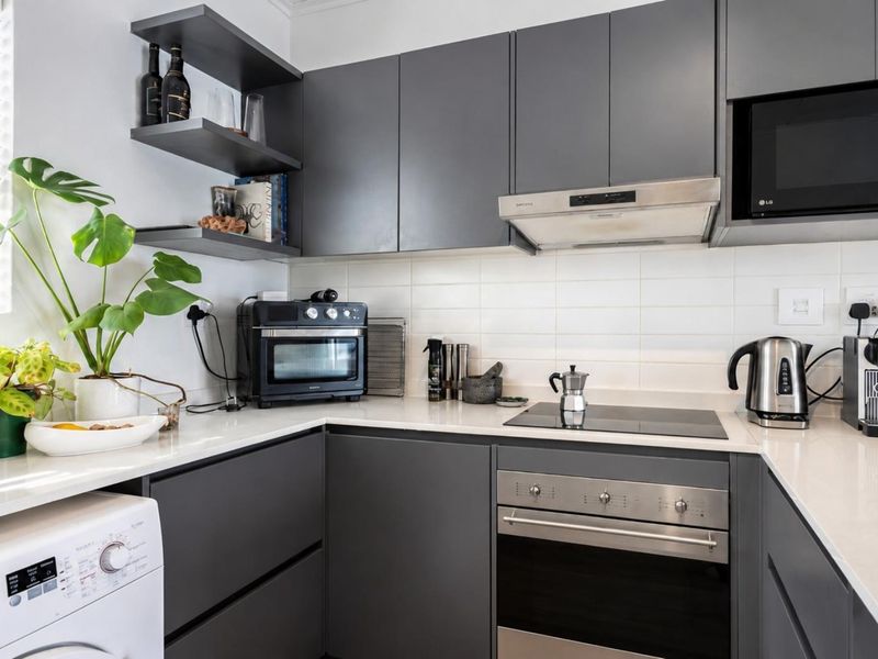 Modern kitchen featuring sleek grey cabinetry, white stone countertops, subway tile backsplash, and integrated appliances including an oven, cooktop, and microwave.