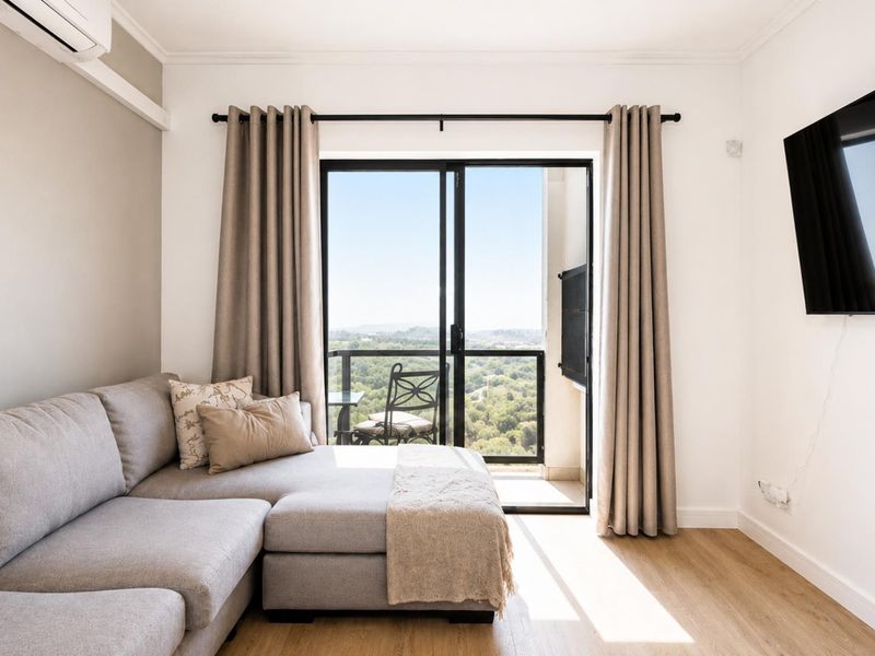 Bright living room featuring laminate flooring, wall-mounted air conditioning, and sliding glass doors leading to a balcony with scenic views.