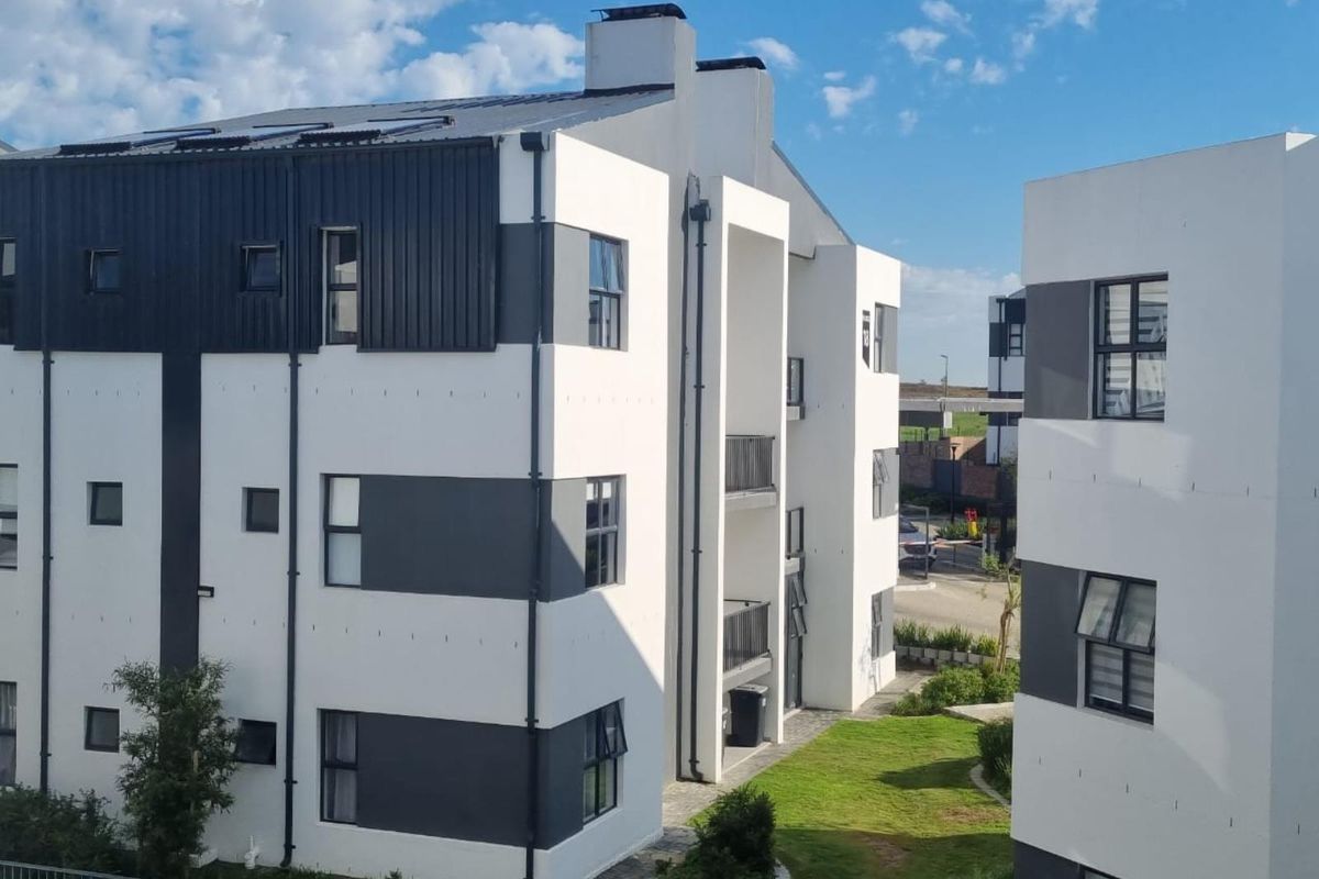 A modern multi-story apartment complex featuring a clean white and grey facade, metal roofing, and well-maintained communal lawn areas.