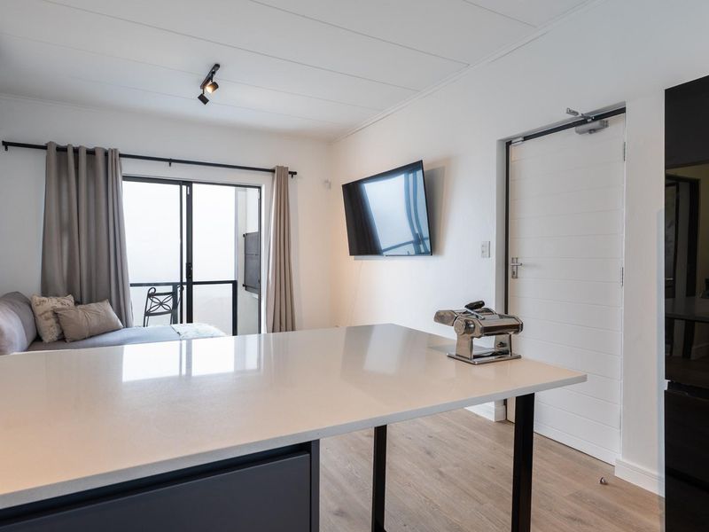 Modern open-plan living area featuring a sleek kitchen island, laminate flooring, split-system air conditioning, and direct access to a private balcony.