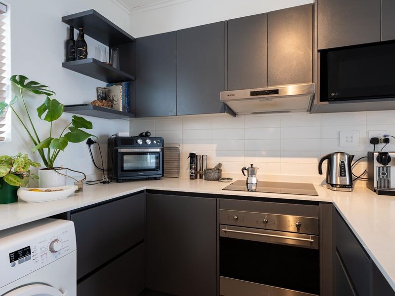 Modern kitchen featuring charcoal cabinetry, white stone countertops, subway tile backsplash, and integrated stainless steel appliances including an oven and extractor fan.
