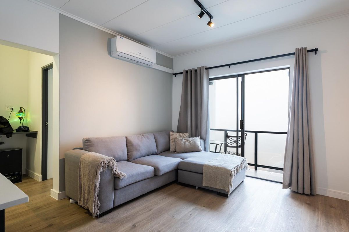A bright living room featuring modern laminate flooring, an air conditioning unit, and direct access to a private balcony through sliding glass doors.