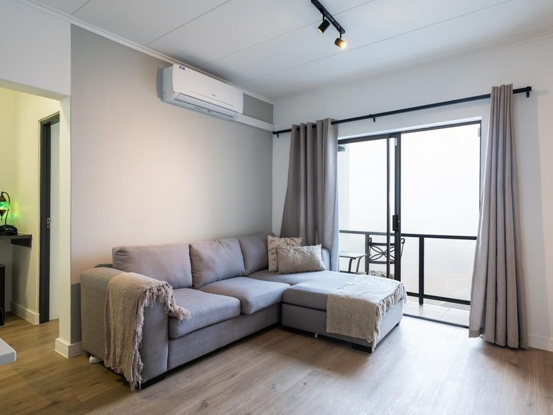 A bright living room featuring modern laminate flooring, an air conditioning unit, and direct access to a private balcony through sliding glass doors.
