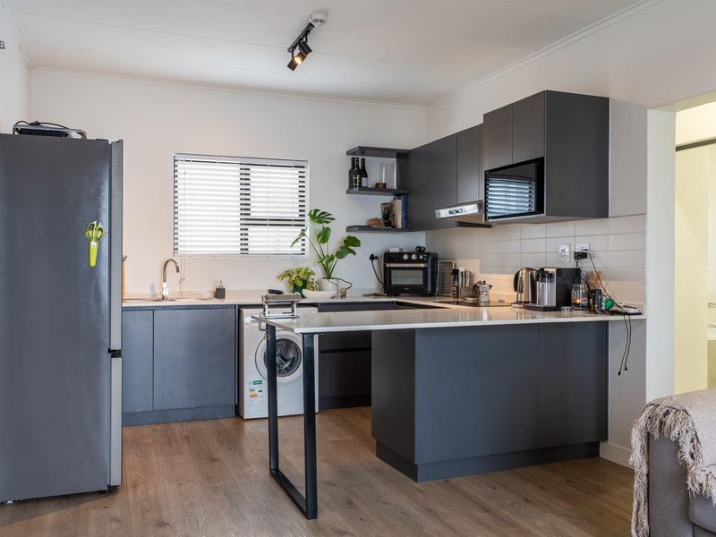 Modern open-plan kitchen featuring dark grey cabinetry, laminate flooring, a breakfast bar, and integrated appliances, creating a functional and stylish living space.