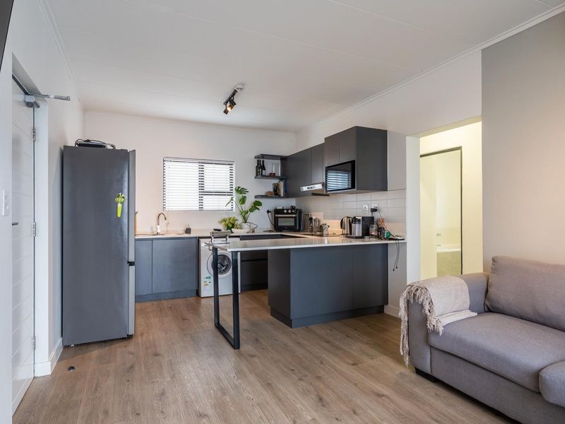 Modern open-plan living area featuring a contemporary kitchen with dark cabinetry, integrated appliances, and durable laminate flooring throughout the space.