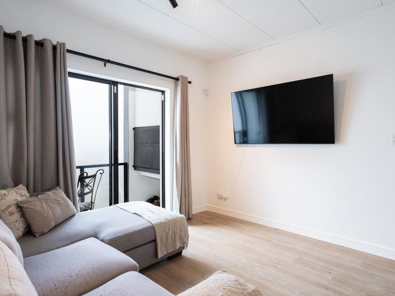 A bright and modern living room featuring laminate flooring, a wall-mounted television, and a sliding glass door providing access to an outdoor area.