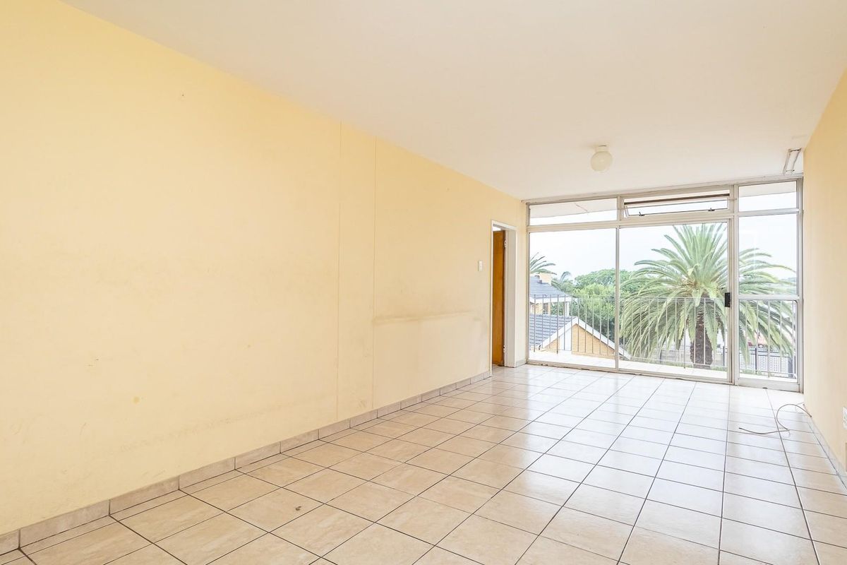 An empty, sunlit living area featuring neutral floor tiles, large sliding glass doors, and access to a balcony with neighborhood views.
