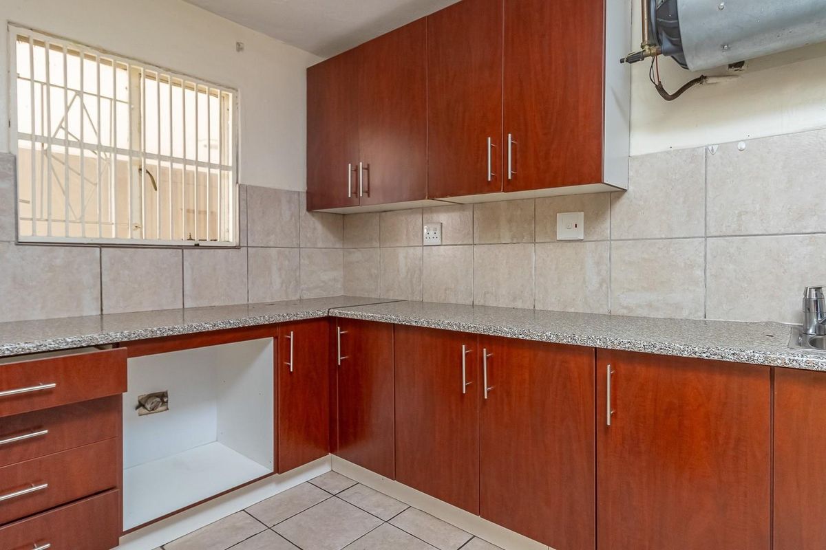A functional kitchen featuring wood-finish cabinetry, granite-look countertops, tiled backsplash, and a stainless steel sink with a window security gate.
