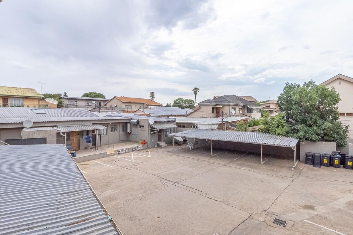 An elevated view of a commercial property courtyard featuring paved parking areas, covered carports, and surrounding building structures.