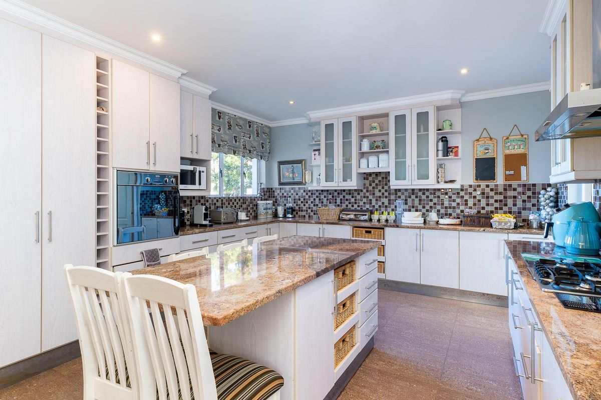 Spacious kitchen featuring light-toned cabinetry, granite countertops, a central island with breakfast seating, and a mosaic tile backsplash.