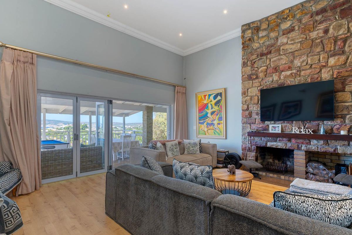 Spacious living room featuring a prominent natural stone fireplace, high ceilings, and large glass sliding doors opening onto a covered patio with scenic views.