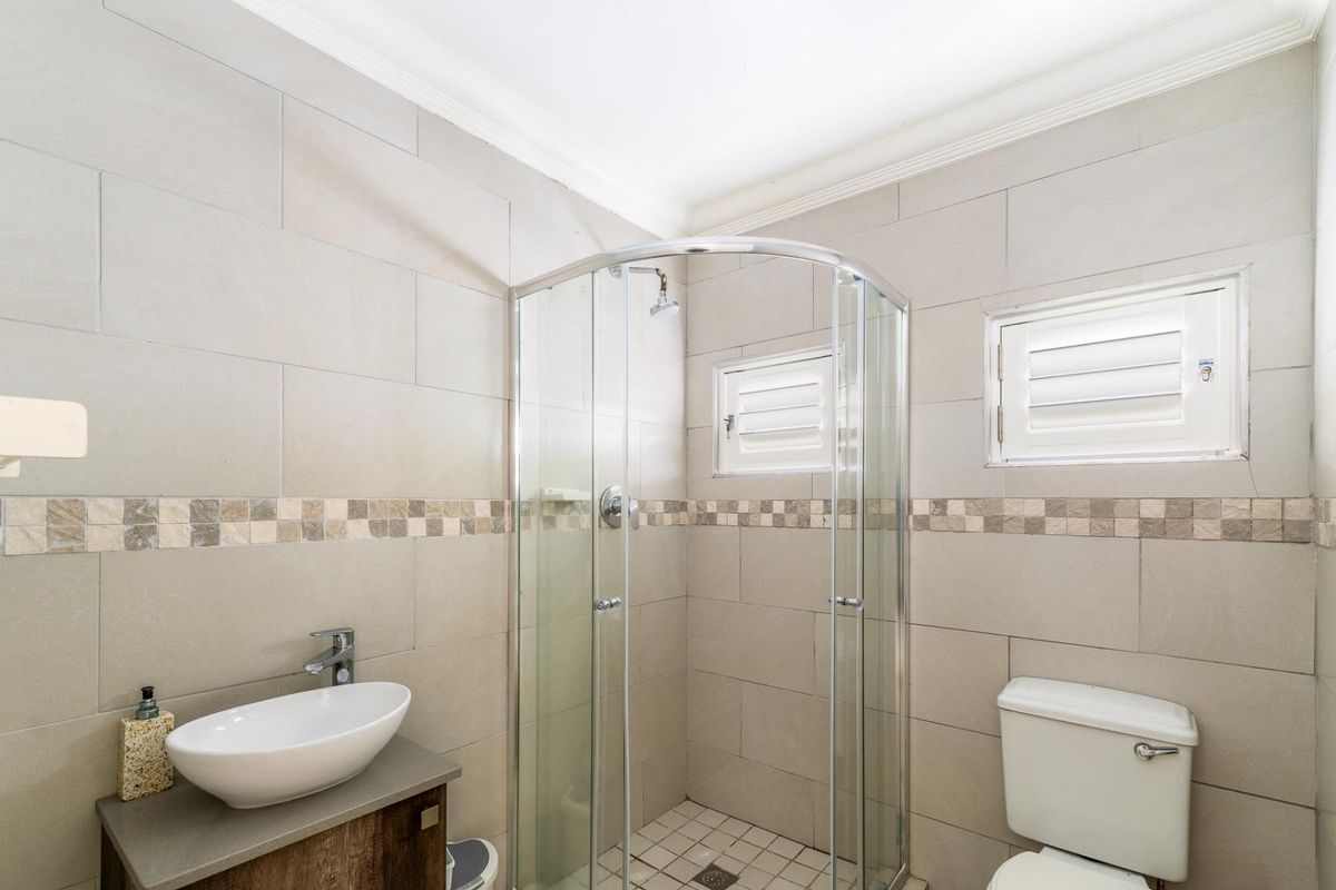 A modern bathroom featuring a glass-enclosed corner shower, a vessel sink vanity, and a toilet, finished with neutral wall tiles and decorative mosaic accents.