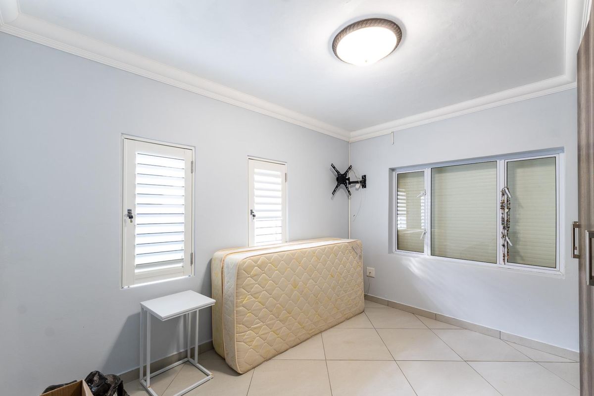 A bedroom featuring tiled flooring, white walls with crown molding, and multiple windows with fitted shutters and blinds.