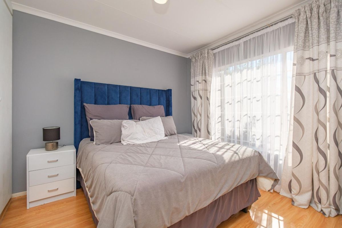 A well-maintained bedroom featuring laminate flooring, neutral grey walls, and large windows with fitted curtain tracks.