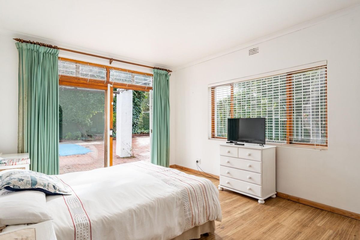 Bright bedroom featuring timber flooring, large windows with blinds, and sliding glass doors providing direct access to the outdoor patio and garden area.