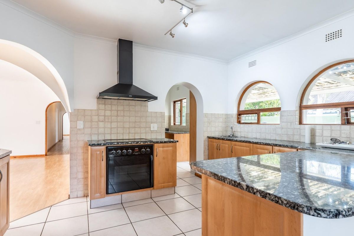 A functional kitchen featuring wooden cabinetry, granite countertops, a built-in oven with extractor fan, and distinctive arched windows.