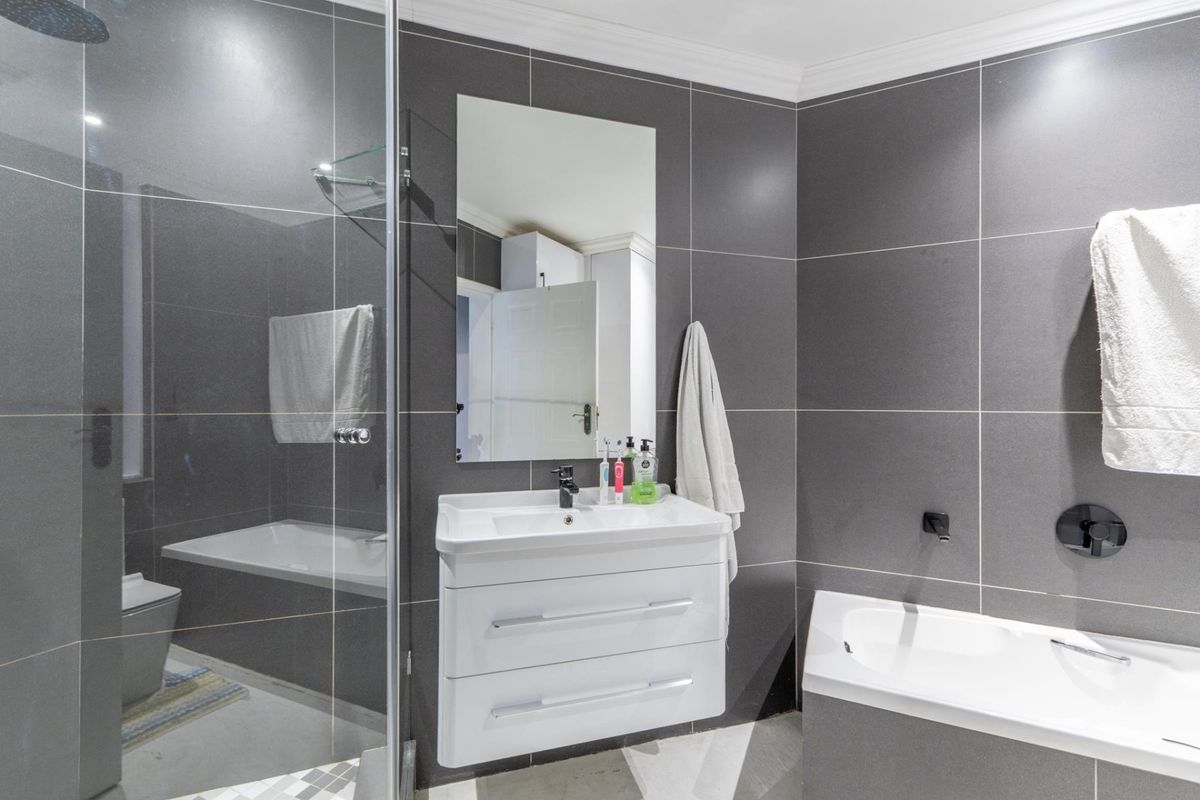 Modern bathroom featuring dark grey wall tiles, a floating vanity with basin, a glass-enclosed shower, and a built-in bathtub.