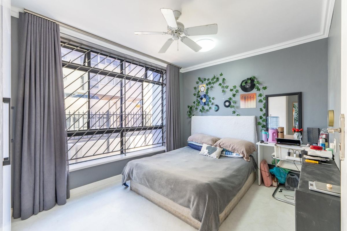 A bedroom featuring a large window with security bars, a ceiling fan, and neutral grey wall tones.