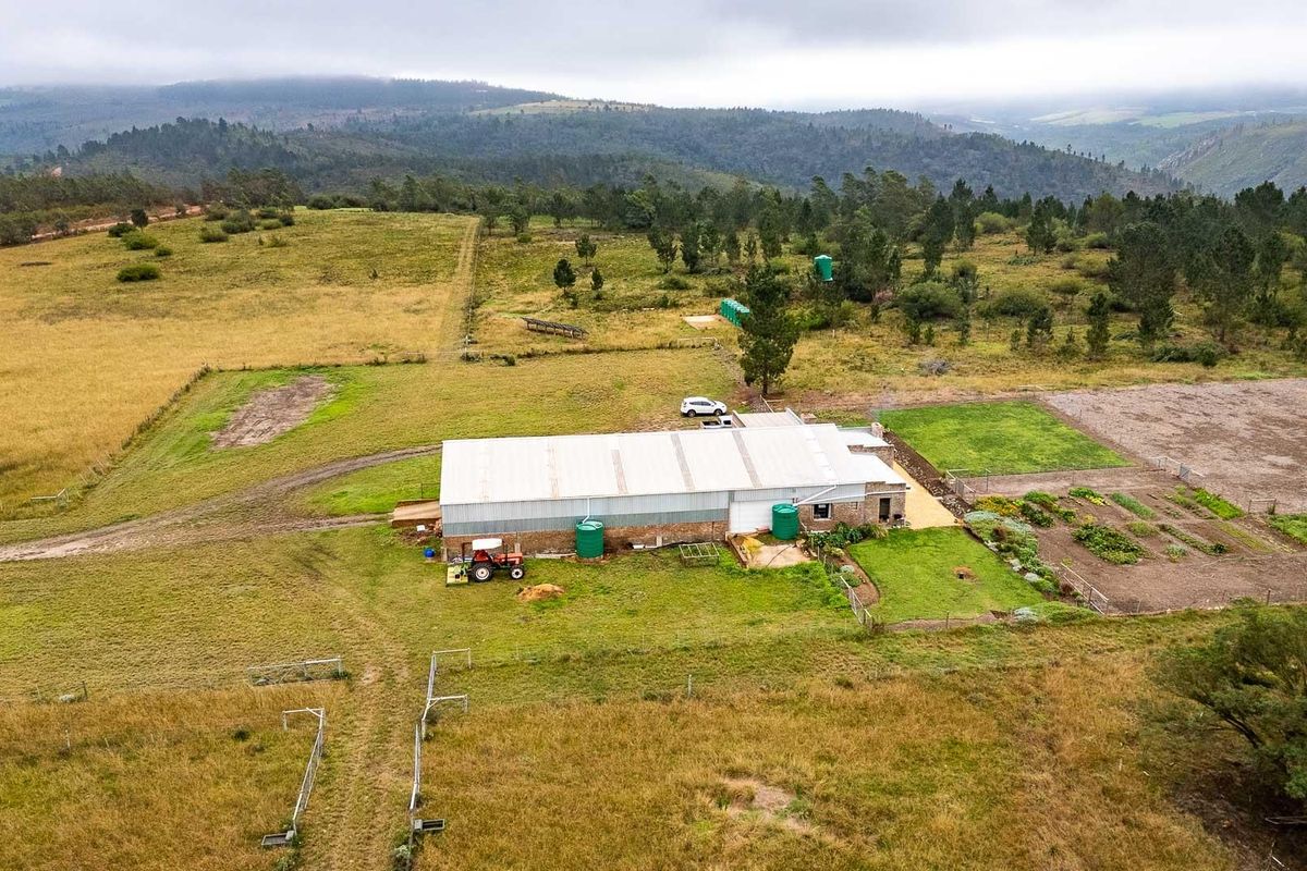 Aerial view of a farm property featuring a large shed, water storage tanks, and surrounding agricultural land with mountain views.