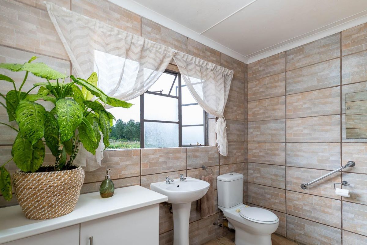 A functional bathroom featuring full-height wall tiling, a pedestal basin, a standard toilet, and a wall-mounted safety grab rail.