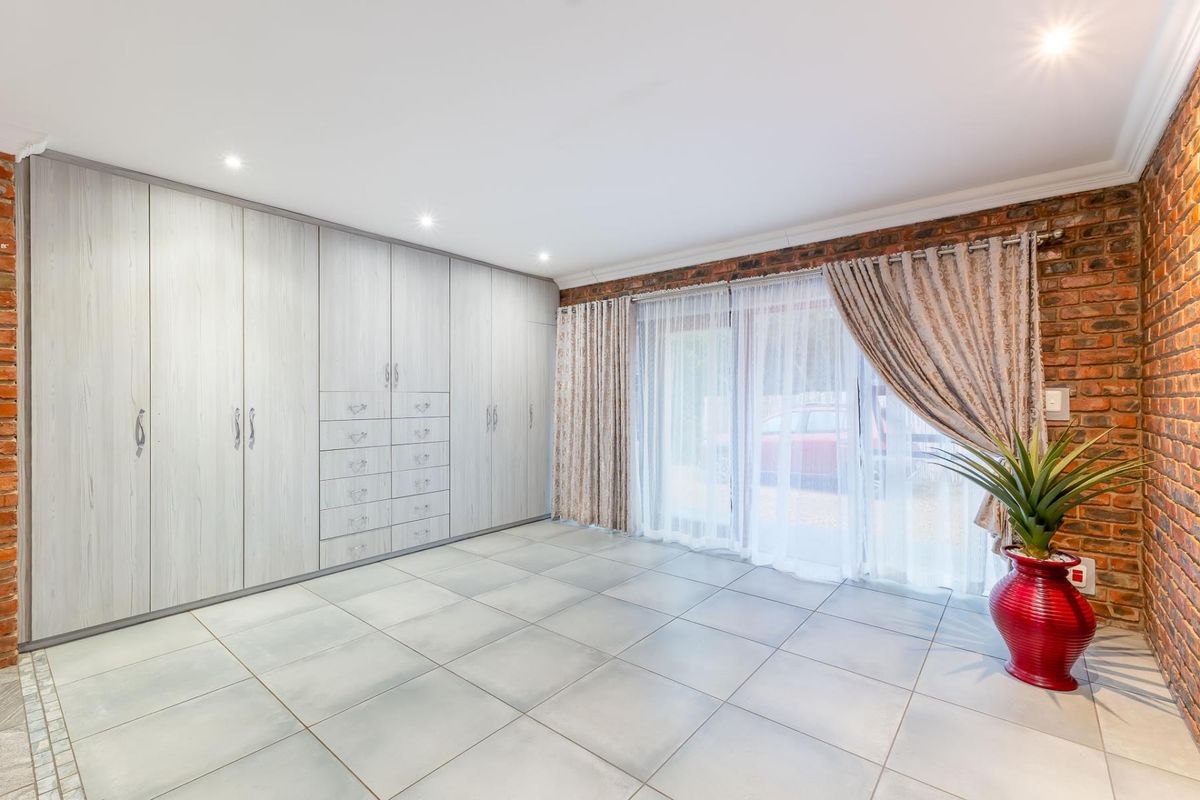 A spacious bedroom featuring extensive built-in cabinetry, tiled flooring, and a feature exposed brick wall with sliding glass doors leading outdoors.