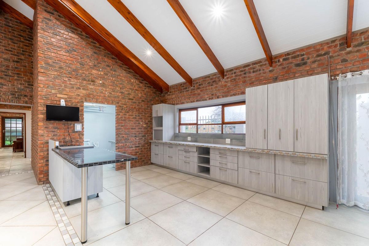 Spacious kitchen featuring exposed brick walls, vaulted timber-beamed ceilings, modern light-toned cabinetry, tiled flooring, and a functional breakfast bar island.
