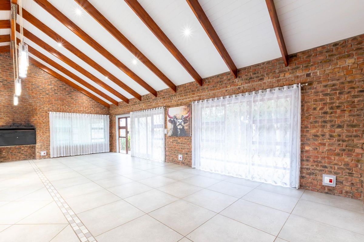Spacious living area featuring exposed brick walls, vaulted ceilings with timber beams, tiled flooring, and large sliding doors providing ample natural light.