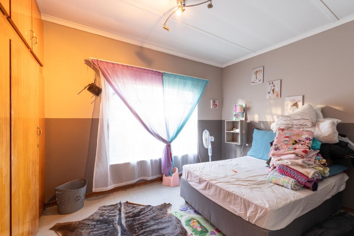 A bedroom featuring built-in wooden cabinetry, tiled flooring, and a large window allowing natural light.