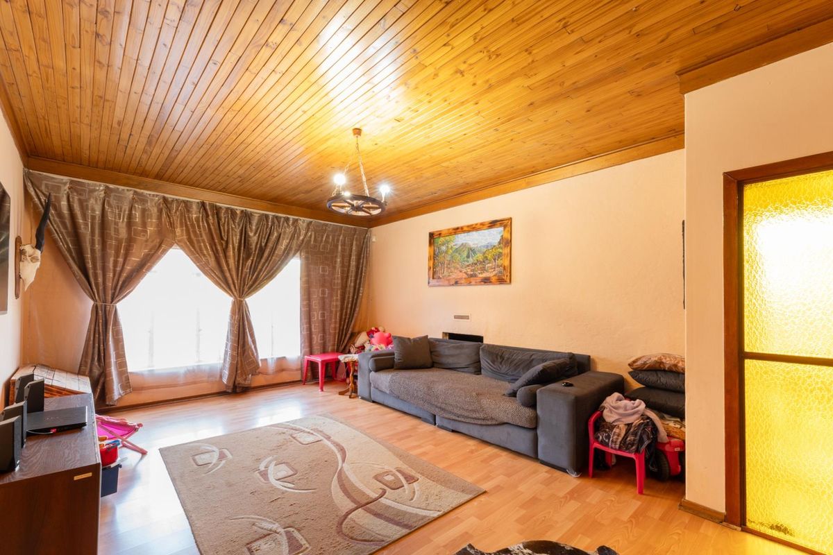 A living room featuring a timber-clad ceiling, laminate flooring, and a large window with natural light.