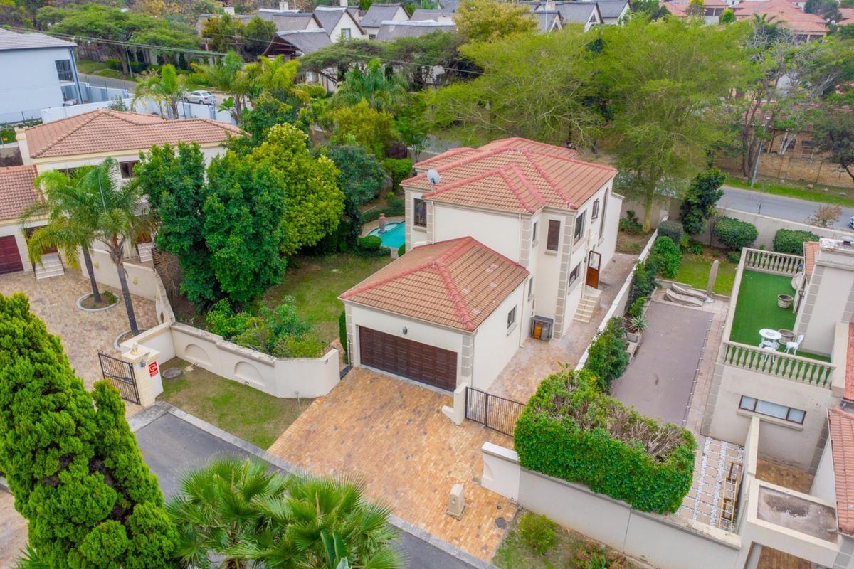 Aerial view of a two-story residential property featuring a tiled roof, paved driveway, attached garage, and a private garden with a swimming pool.