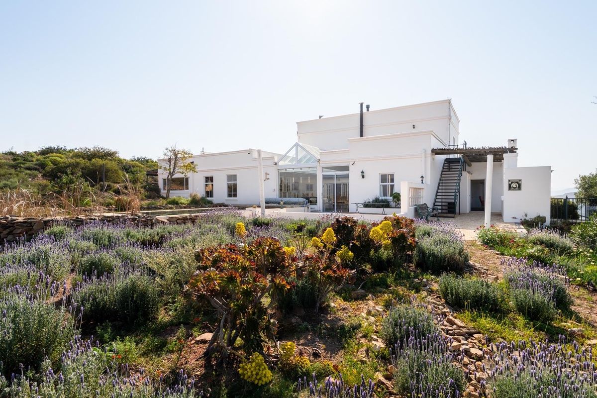 Rear view of a white farmhouse featuring a glass conservatory, external staircase, and a landscaped garden with stone retaining walls.