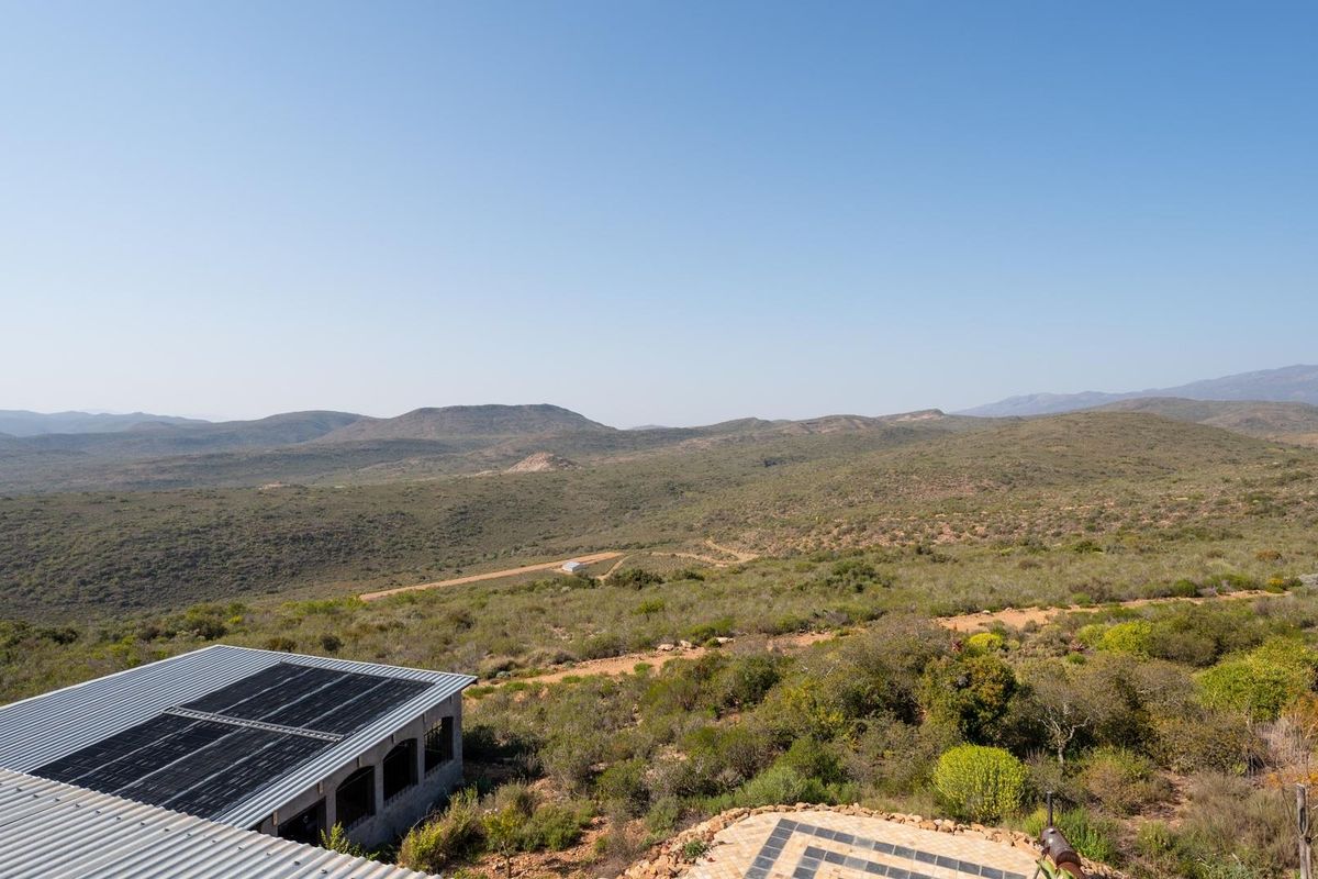 An elevated aerial view of the property showcasing the expansive rural landscape, solar panel installation on the roof, and a paved outdoor patio area.