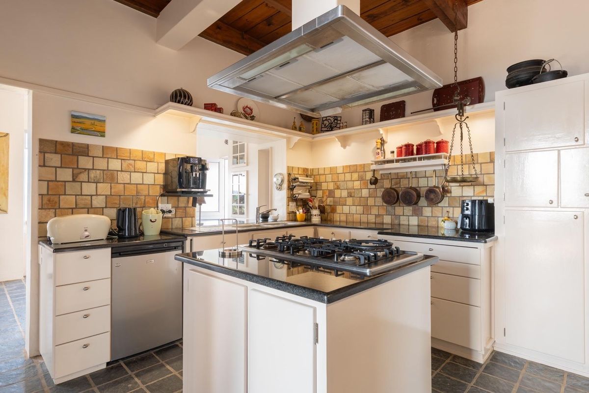 A rustic-style kitchen featuring a central island with a gas cooktop, stone countertops, tiled backsplash, and exposed timber ceiling beams.