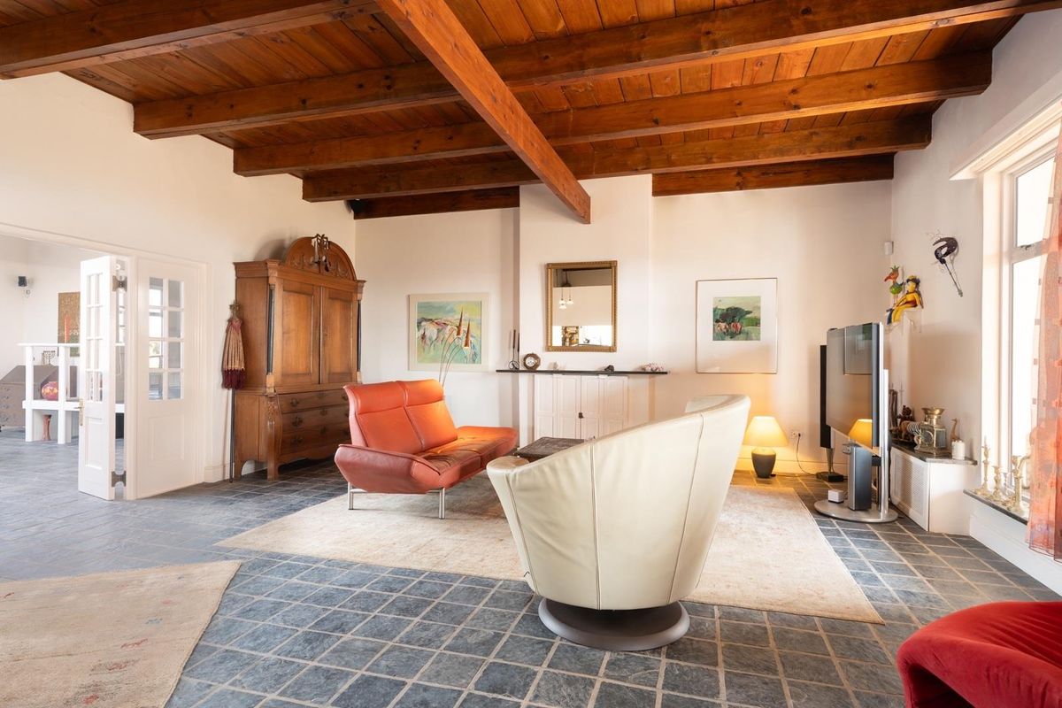 Spacious living room featuring exposed timber ceiling beams, stone tile flooring, and a central fireplace mantle, offering a rustic and character-filled atmosphere.