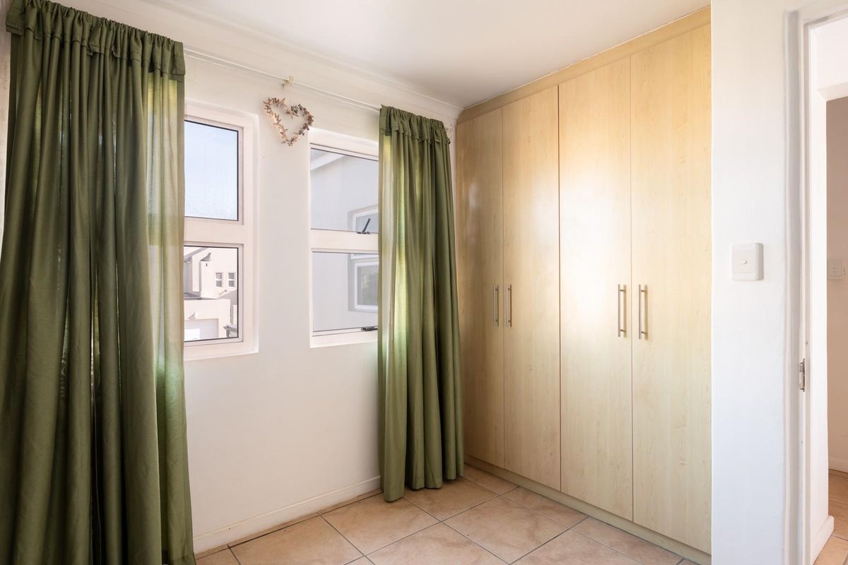 A bedroom featuring built-in light wood cabinetry, tiled flooring, and dual windows with curtains.