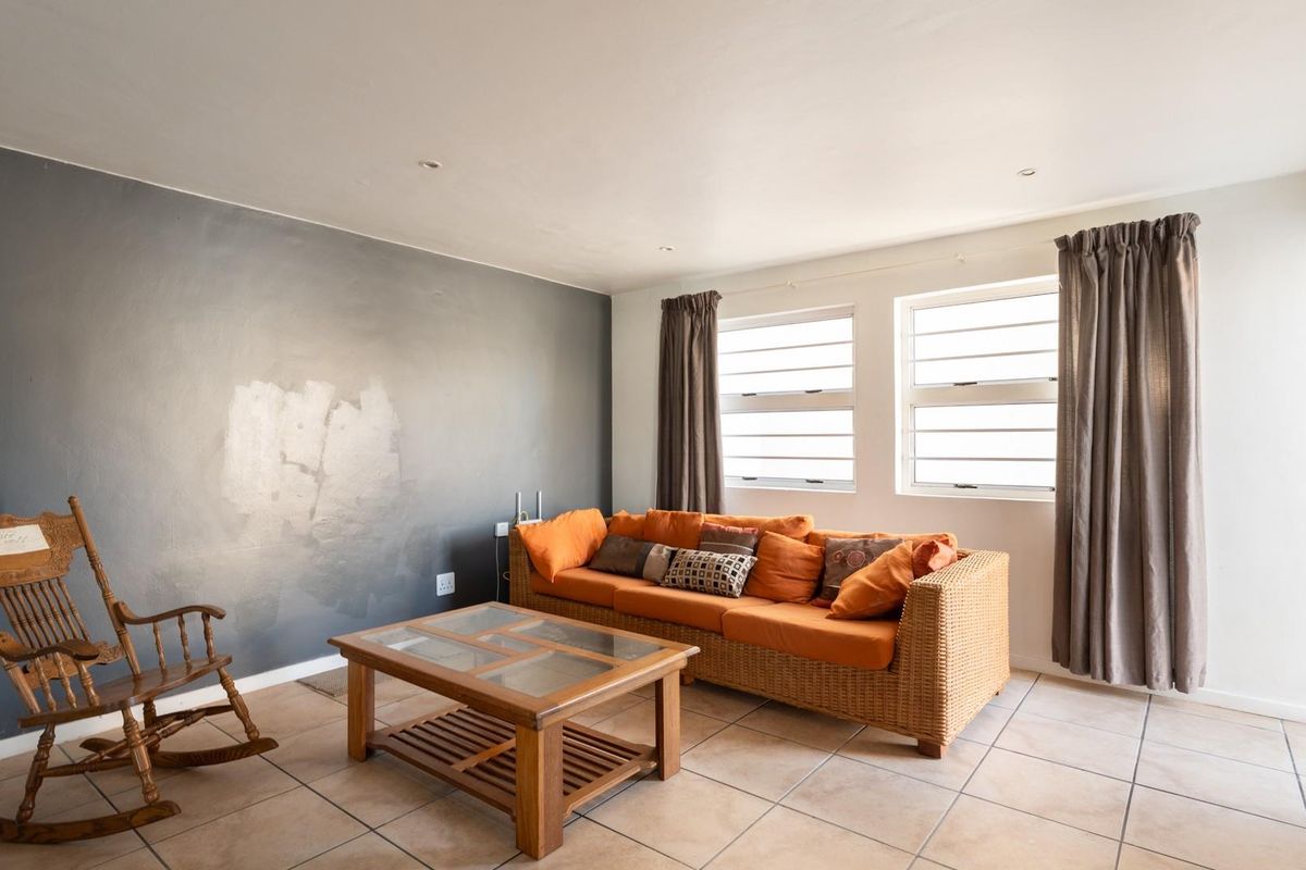 A living room featuring tiled flooring, recessed ceiling lighting, and a dark grey accent wall with visible paint imperfections.