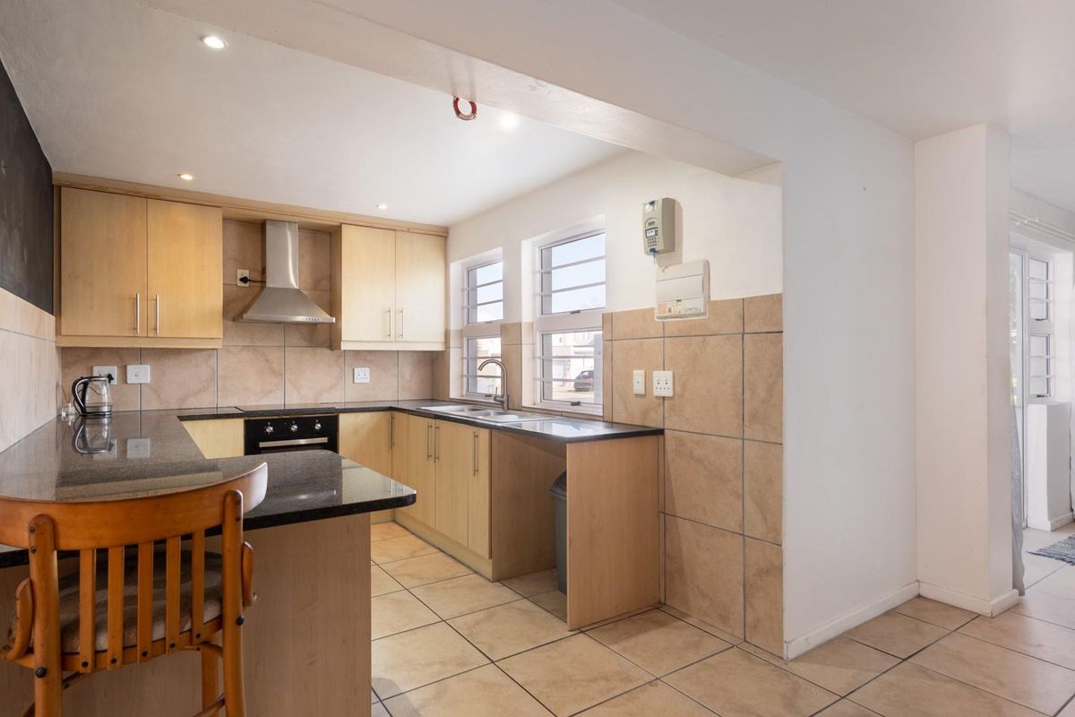 Functional kitchen featuring light wood cabinetry, dark granite countertops, stainless steel extractor fan, and tiled flooring with an integrated breakfast bar.