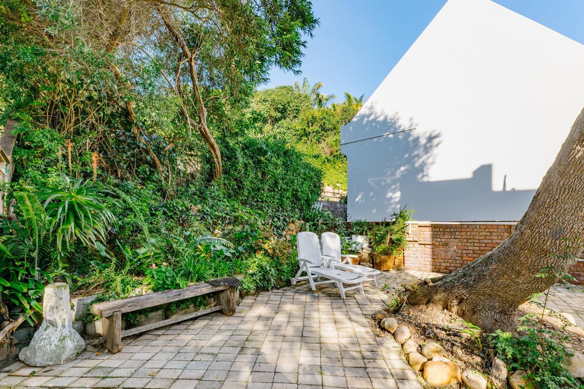 A private rear garden area featuring a paved patio, brick retaining wall, and established trees, providing a tranquil outdoor space.