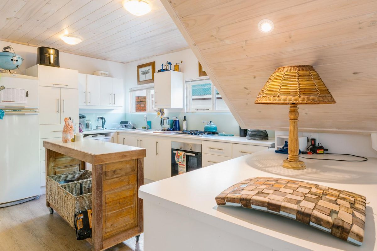 A functional kitchen featuring white cabinetry, built-in oven and hob, timber-clad ceiling, and a central island unit under a sloped roof section.