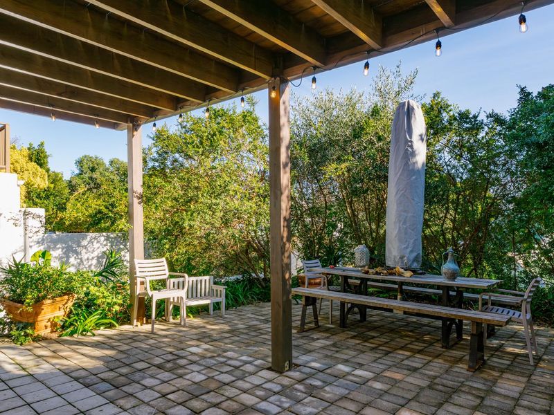A covered outdoor patio featuring a timber pergola, paved flooring, and integrated string lighting, overlooking a lush garden area.