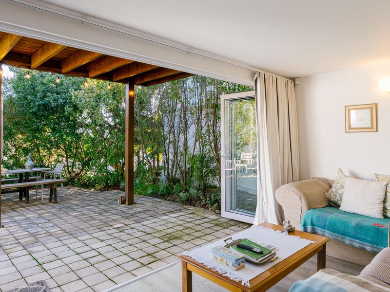 Open plan living area featuring large sliding glass doors that open onto a covered timber pergola and paved patio space.