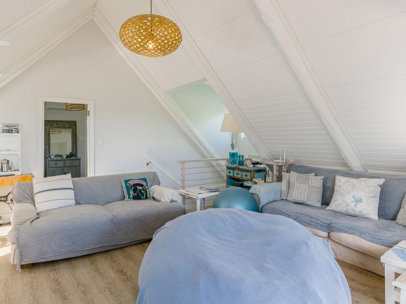 A bright, spacious living area featuring a high vaulted ceiling with exposed timber beams and light-toned timber-look flooring.