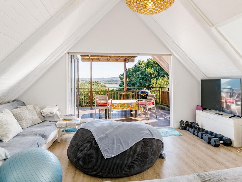 Spacious living area with vaulted ceilings and timber flooring, featuring large sliding doors that open onto an elevated timber deck with scenic views.