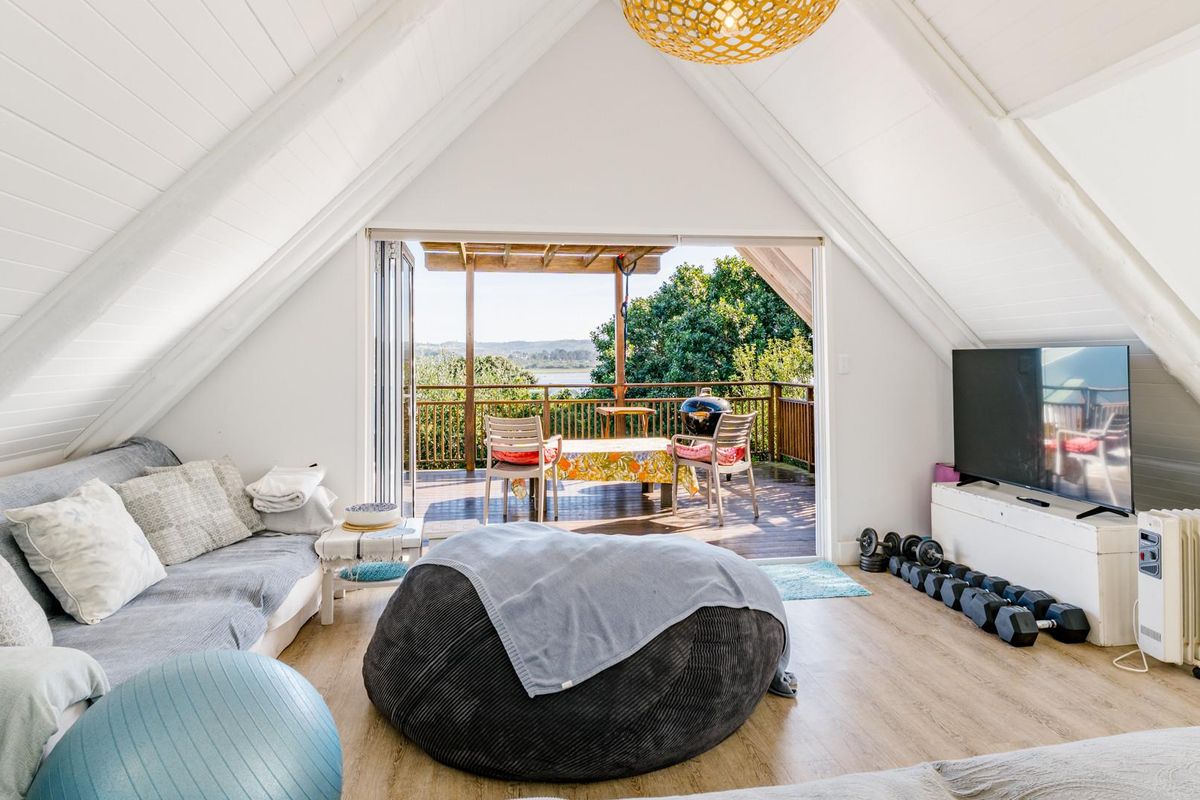 Spacious living area with vaulted ceilings and timber flooring, featuring large sliding doors that open onto an elevated timber deck with scenic views.