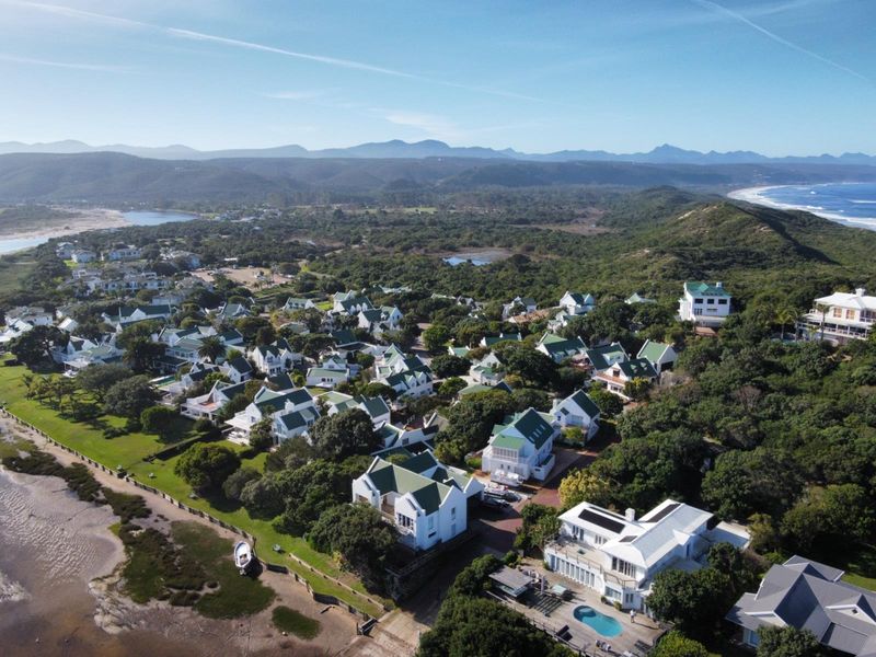 An aerial view of a coastal residential estate featuring multiple homes with pitched roofs, swimming pools, and surrounding natural vegetation near the shoreline.