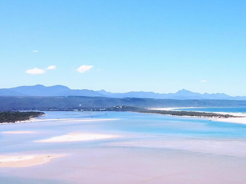 A scenic panoramic view of the coastal estuary, sandbanks, and distant mountain range under a clear blue sky.